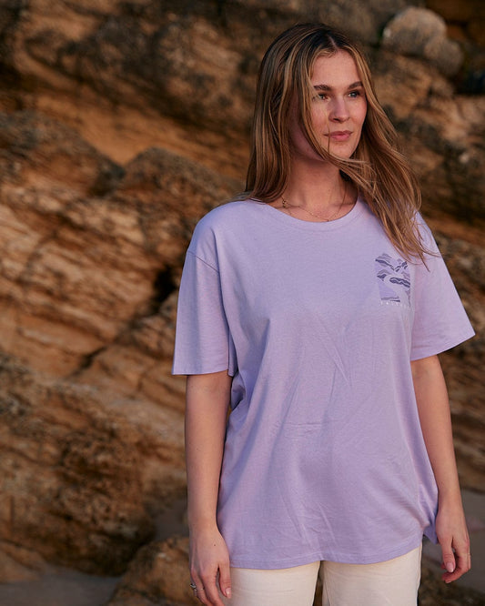 A woman wearing a Saltrock Live Wild - Womens Short Sleeve T-Shirt - Light Purple standing on a rock.