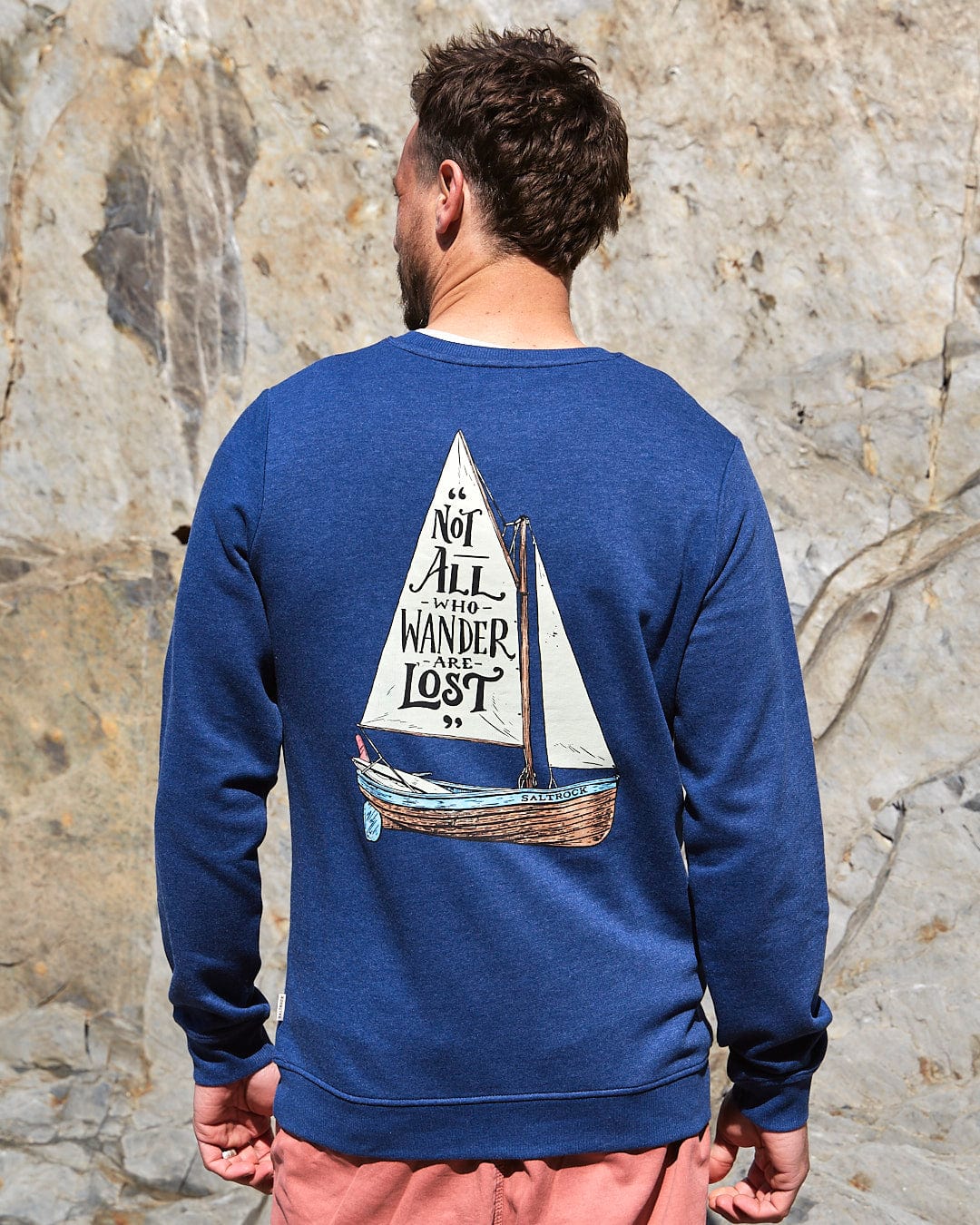 A man wearing a Saltrock sweatshirt with the Lost Ships - Mens Crew Sweat - Dark Blue design, featuring a sailboat on it.
