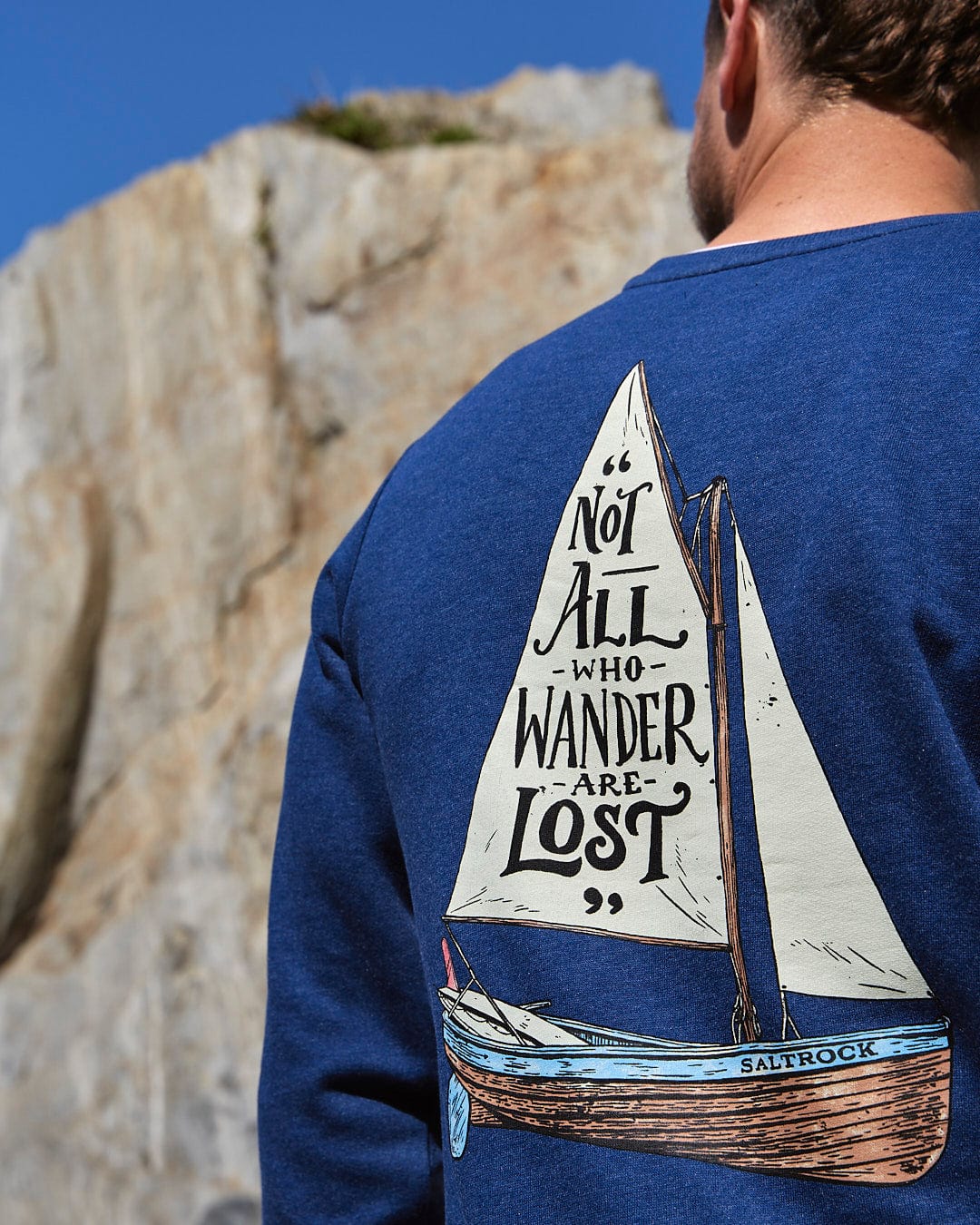 A man wearing a Saltrock Lost Ships - Mens Crew Sweat - Dark Blue sweatshirt with a sailboat on it.
