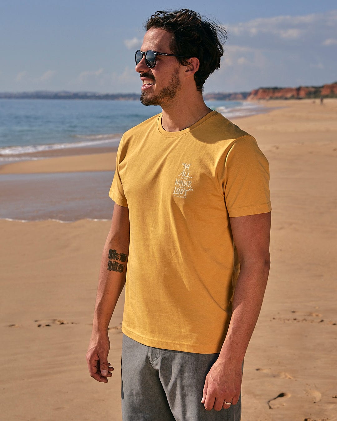 A man wearing a Lost Ships - Mens Short Sleeve T-Shirt - Yellow by Saltrock standing on the beach.