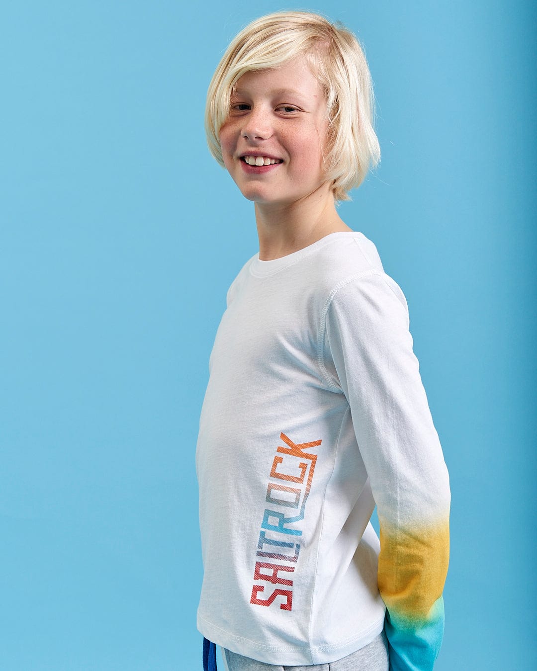 A young boy wearing a Saltrock Marcus - Kids Long Sleeve Dip Dye T-Shirt in White.