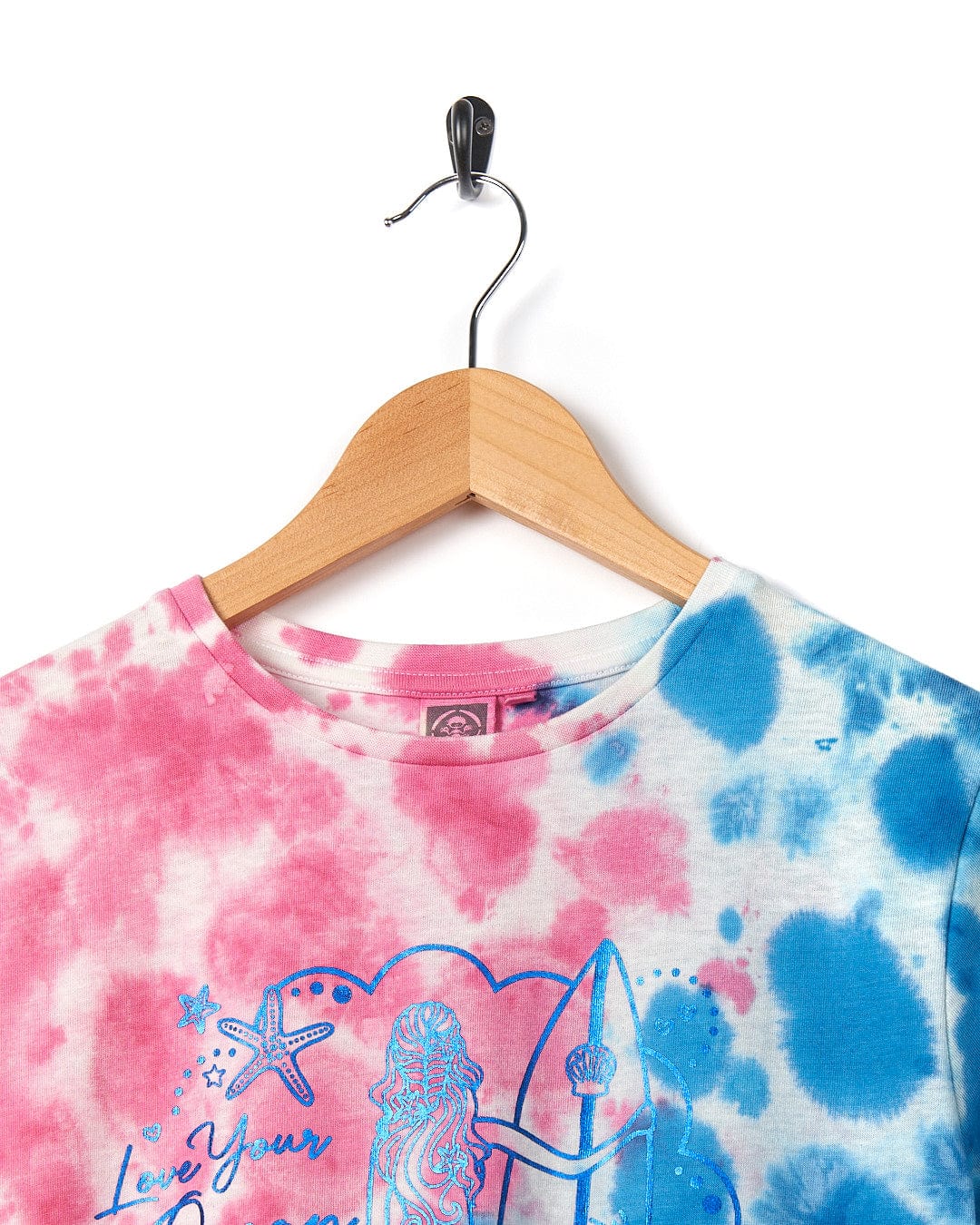 A Saltrock Mermaid Surf - Kids Tie Dye Short Sleeve T-Shirt - Blue/Pink, beach ready with a tie dye design and an image of a girl riding a surfboard.