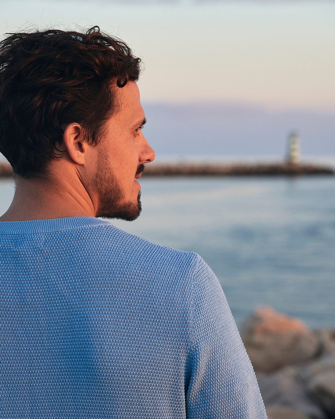 A man looking out over the water wearing Moss - Mens Washed Knitted Crew in Light Blue by Saltrock.