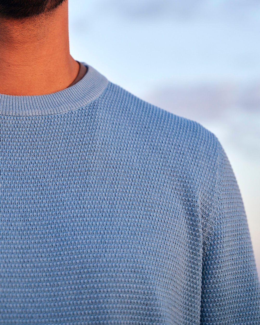 A close up of a man wearing the Saltrock Moss - Mens Washed Knitted Crew - Light Blue sweater.