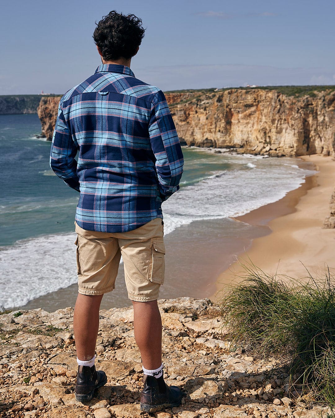 A man wearing the Saltrock Ocean - Mens Borg Lined Shirt - Blue Check standing on a cliff overlooking the ocean in winter.