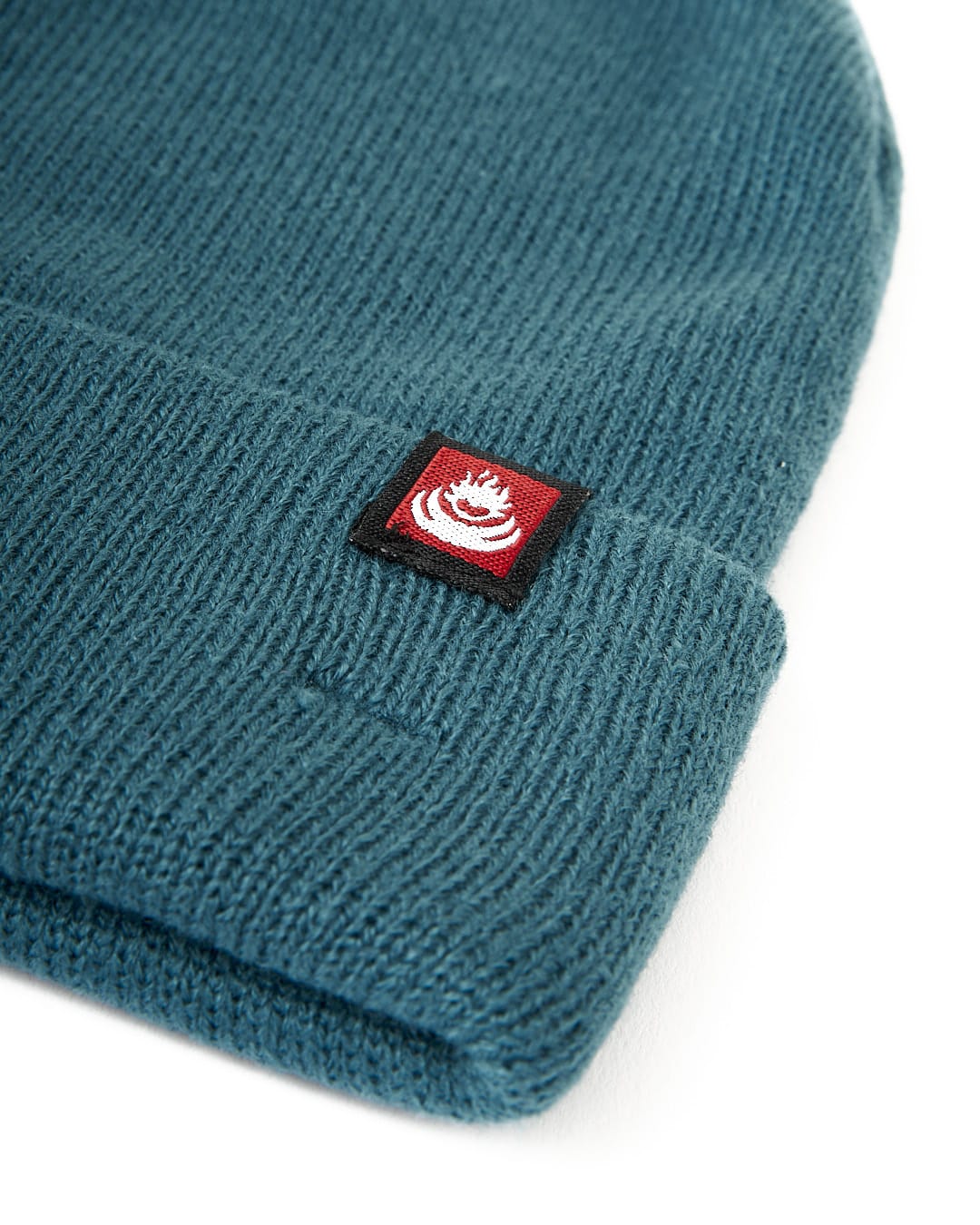 A Saltrock Tight Knit Beanie in Teal with a red logo, perfect for staying cozy in the winter.
