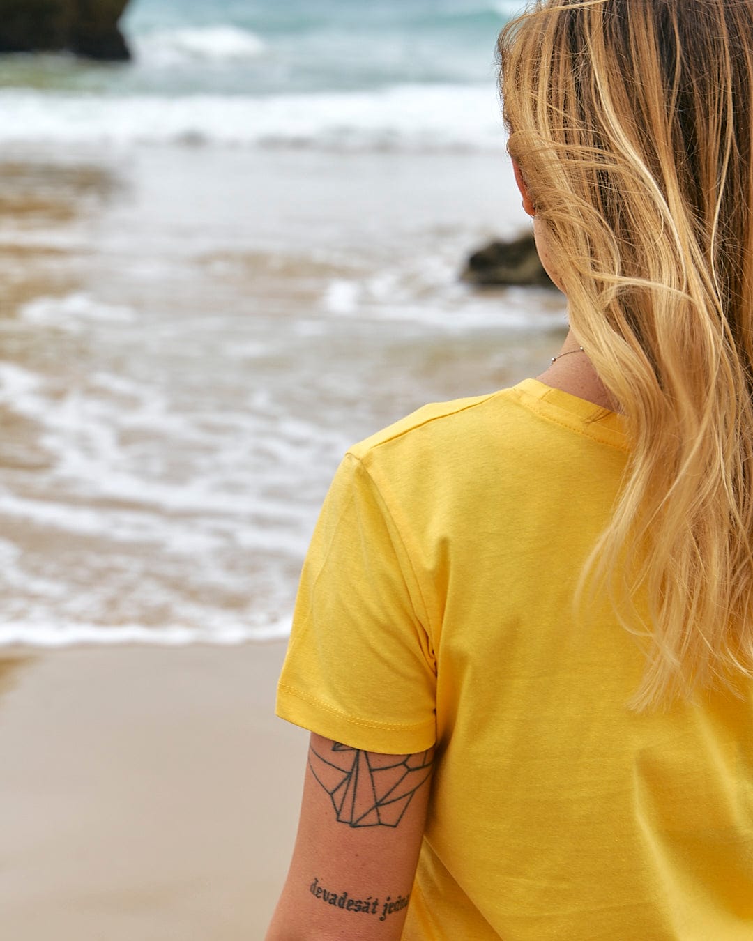 A woman wearing a Saltrock On The Road - Womens Short Sleeve T-Shirt - Yellow looking at the ocean.