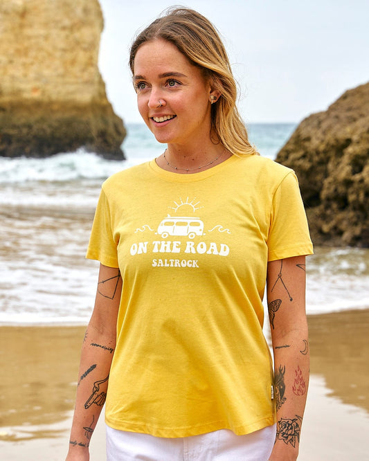 A woman wearing a Saltrock On The Road - Womens Short Sleeve T-Shirt - Yellow on the beach.