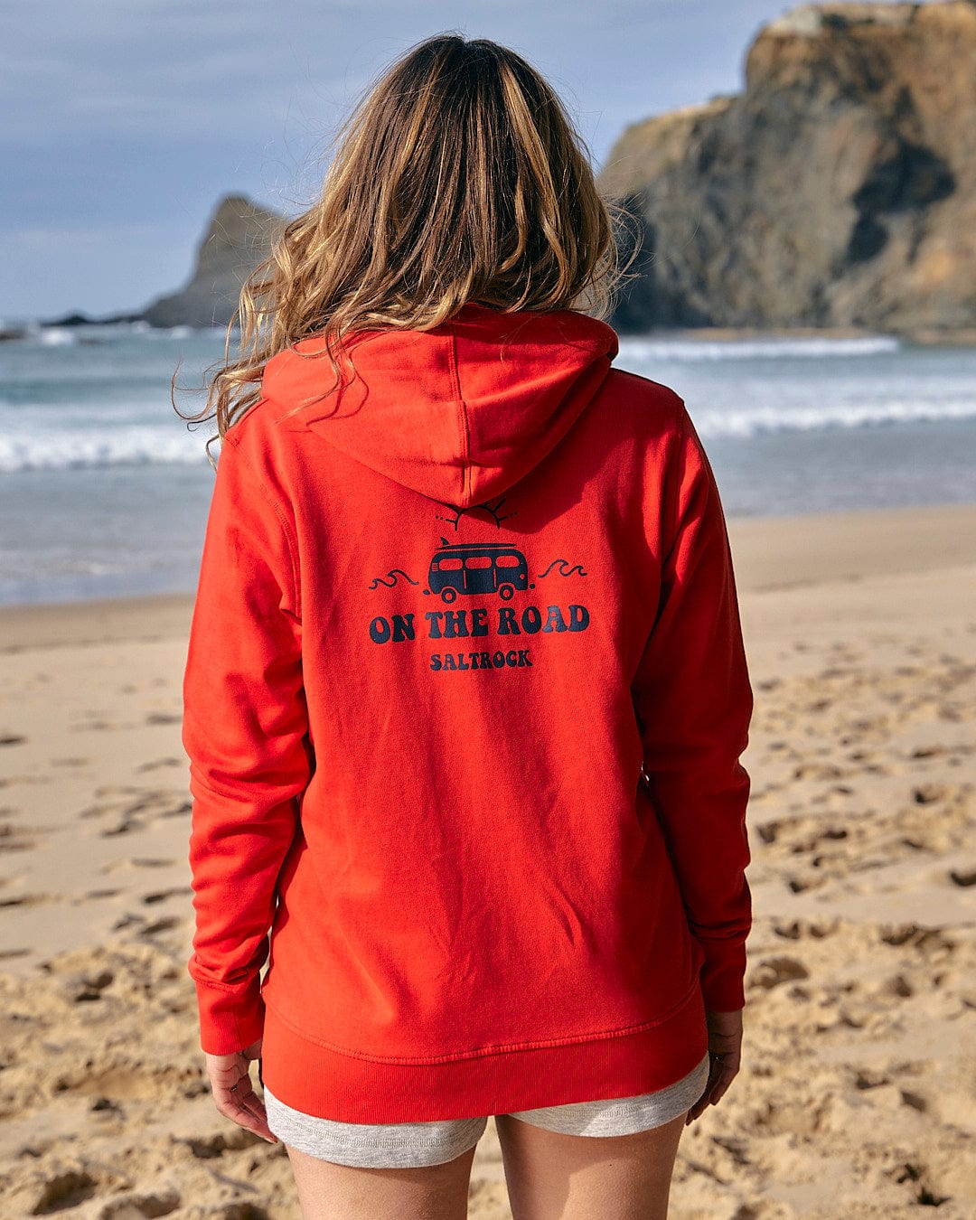 The back of a woman wearing a Saltrock On The Road - Womens Zip Hoodie - Red on the beach.