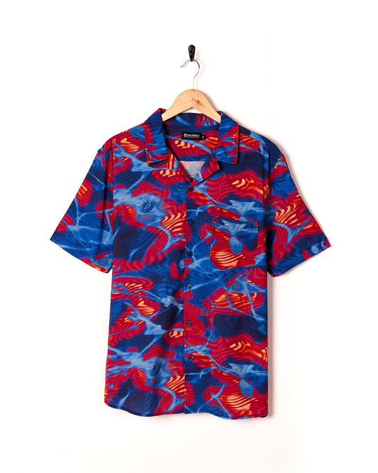 A Saltrock Poolside - Mens Short Sleeve Shirt in a bright and fun blue and red Hawaiian print, made of lightweight fabric, hanging on a hanger.