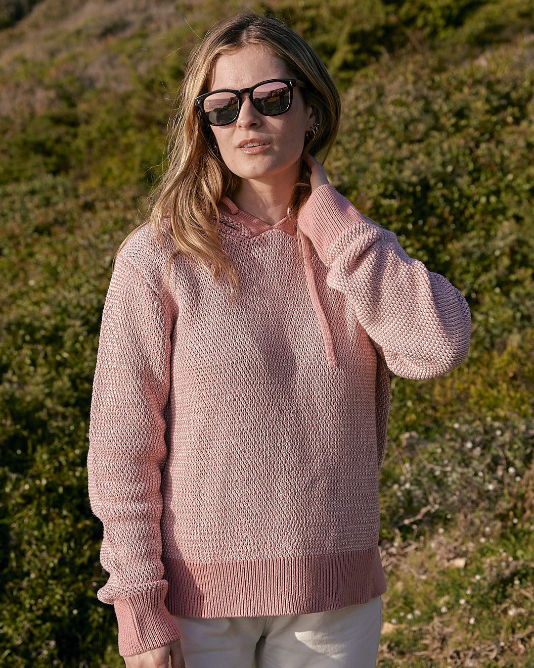 A woman wearing a Saltrock Poppy - Womens Knitted Pop Hoodie - Mid Pink sweater and sunglasses.