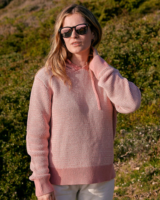 A woman wearing a Saltrock Poppy - Womens Knitted Pop Hoodie - Mid Pink sweater and sunglasses.
