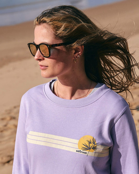 A woman wearing Saltrock sunglasses and a Saltrock Poster Stripe - Womens Crew Sweat - Light Purple on the beach.