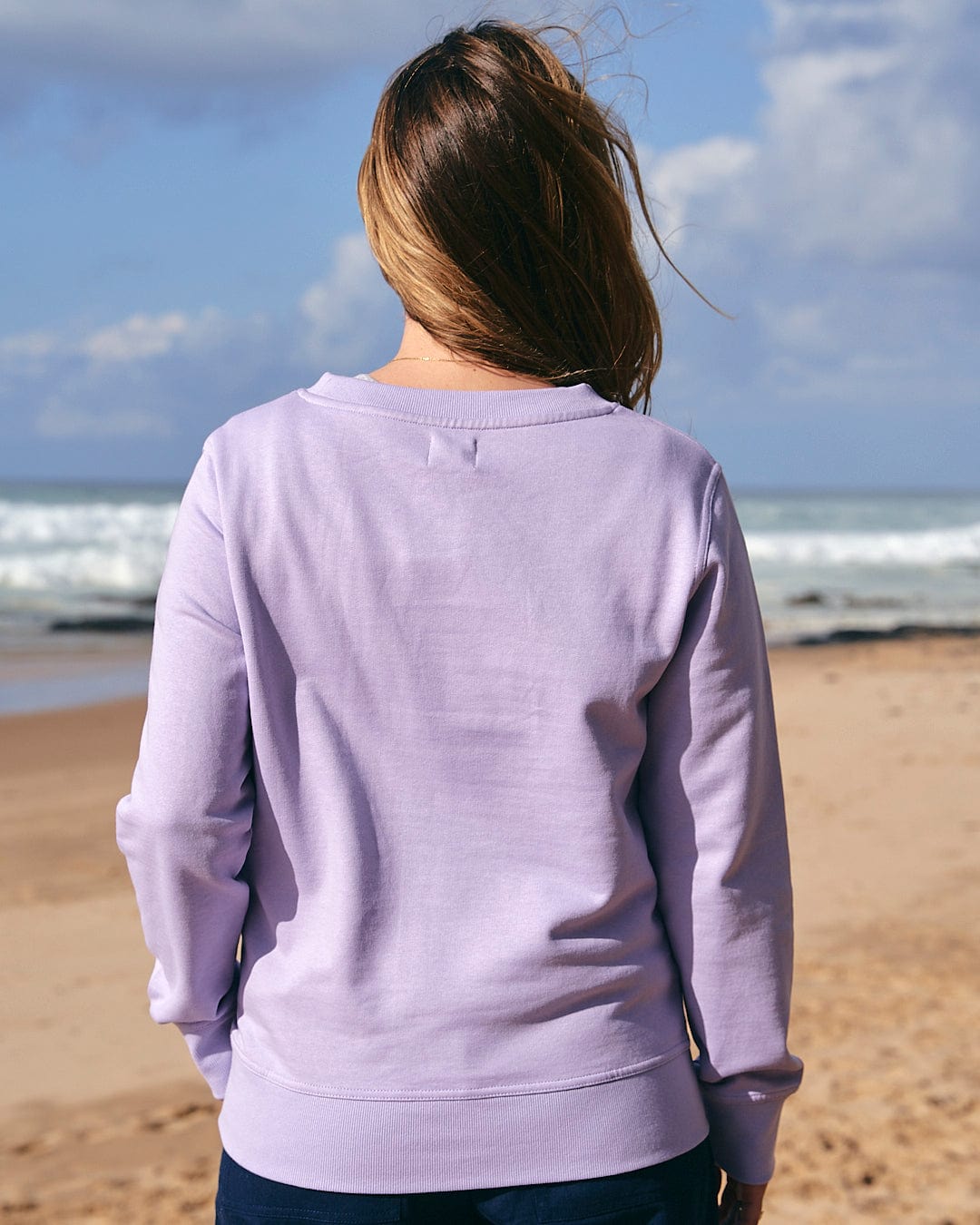 The back of a woman wearing a Saltrock Poster Stripe - Womens Crew Sweat - Light Purple on the beach.
