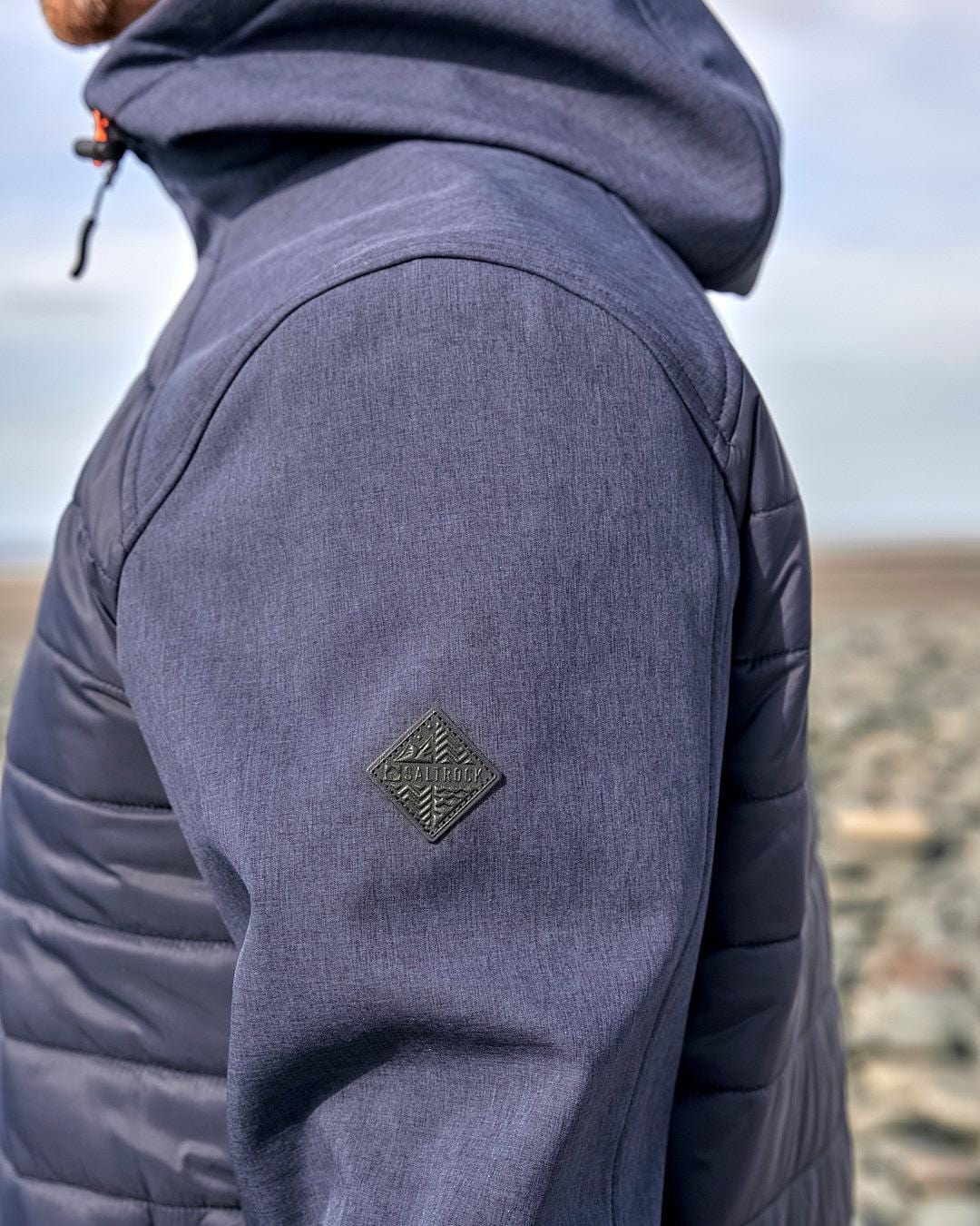 The back of a man in a Saltrock Purbeck Padded Jacket - Dark Blue standing on the beach.