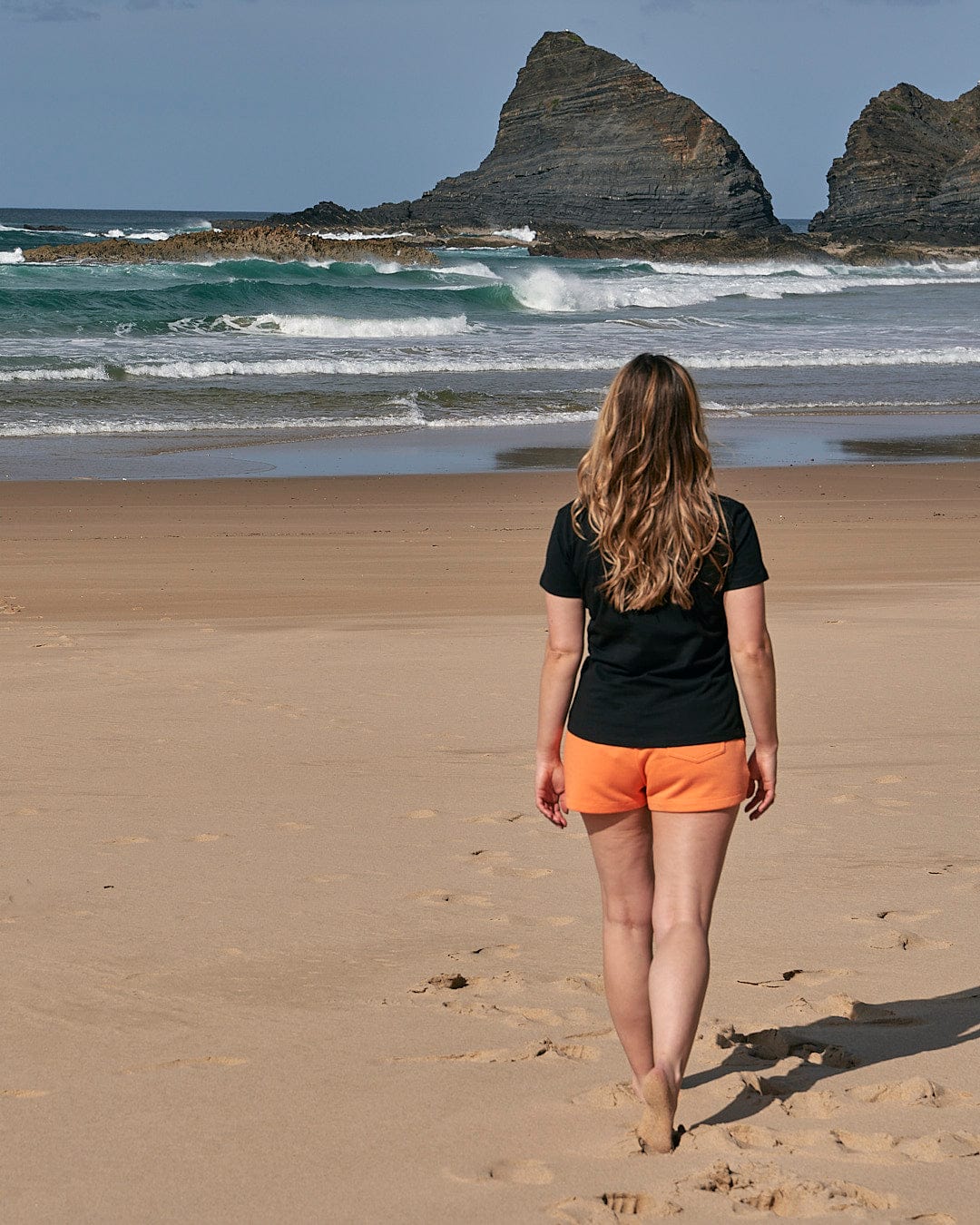 A woman walking on a beach wearing the Purfect Wave Gradient - Womens Short Sleeve T-Shirt in Black by Saltrock.