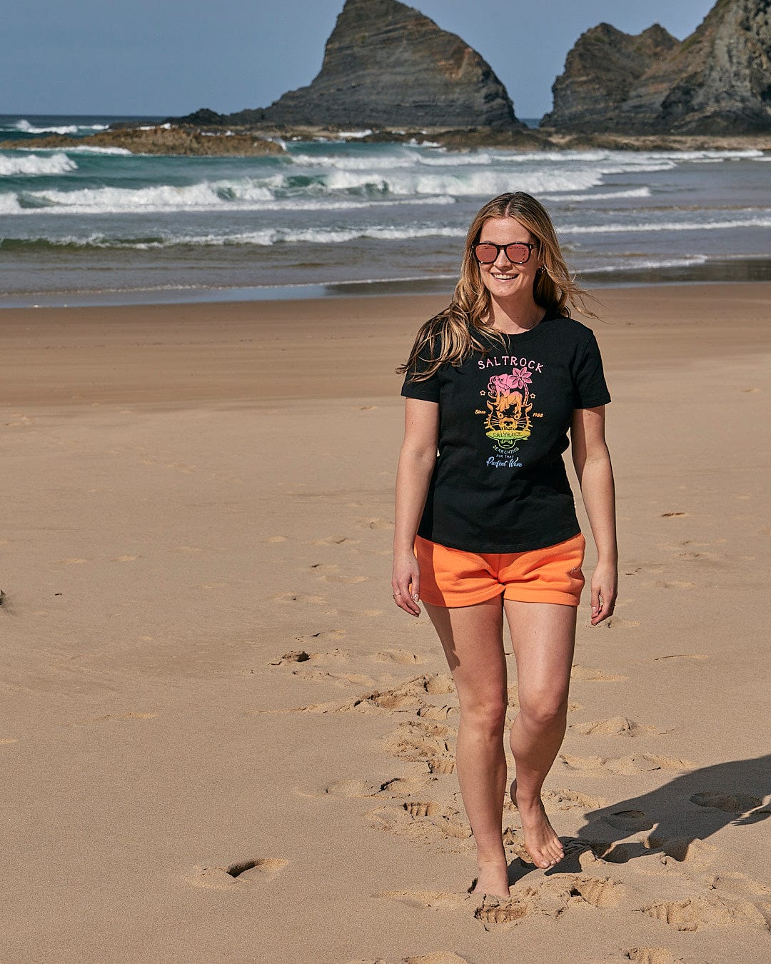 A woman walking on the beach wearing a Saltrock Purfect Wave Gradient - Womens Short Sleeve T-Shirt in Black.
