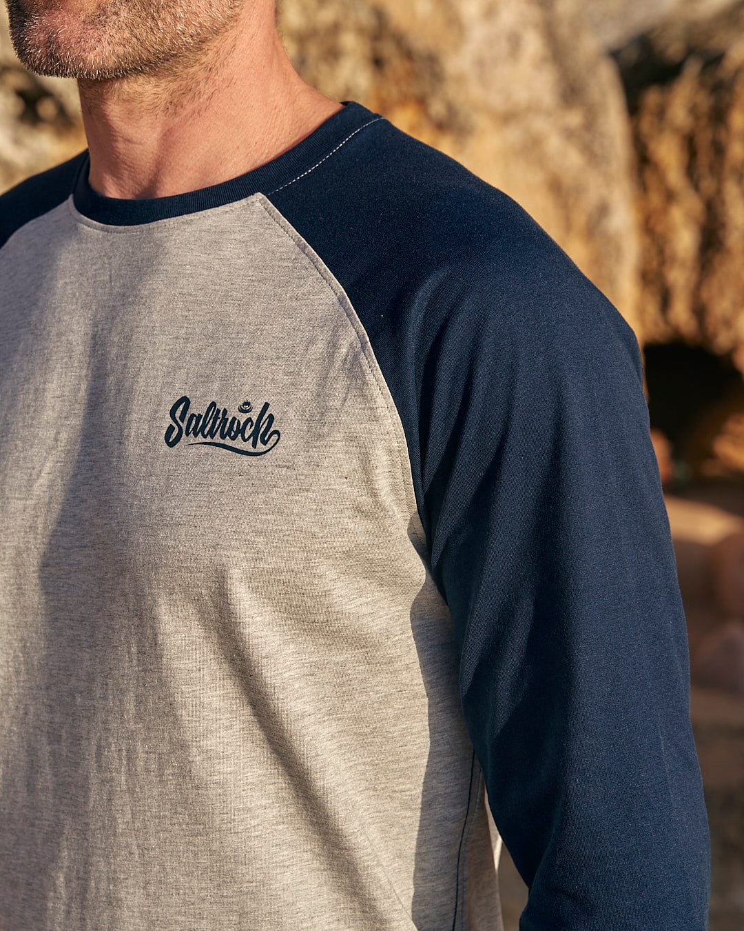 A man wearing a grey and navy Saltrock Speed - Mens Long Sleeve Raglan T-Shirt - Blue.