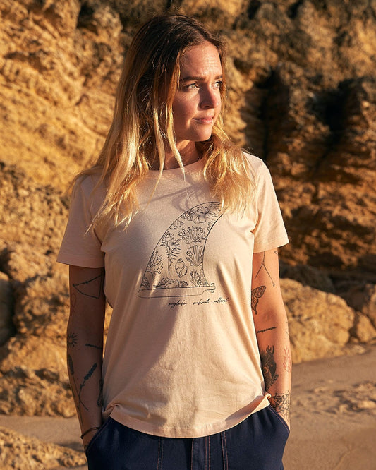 A woman wearing a Summer Fin - Womens Short Sleeve T-Shirt - Cream by Saltrock with a summer look standing on a rocky beach.