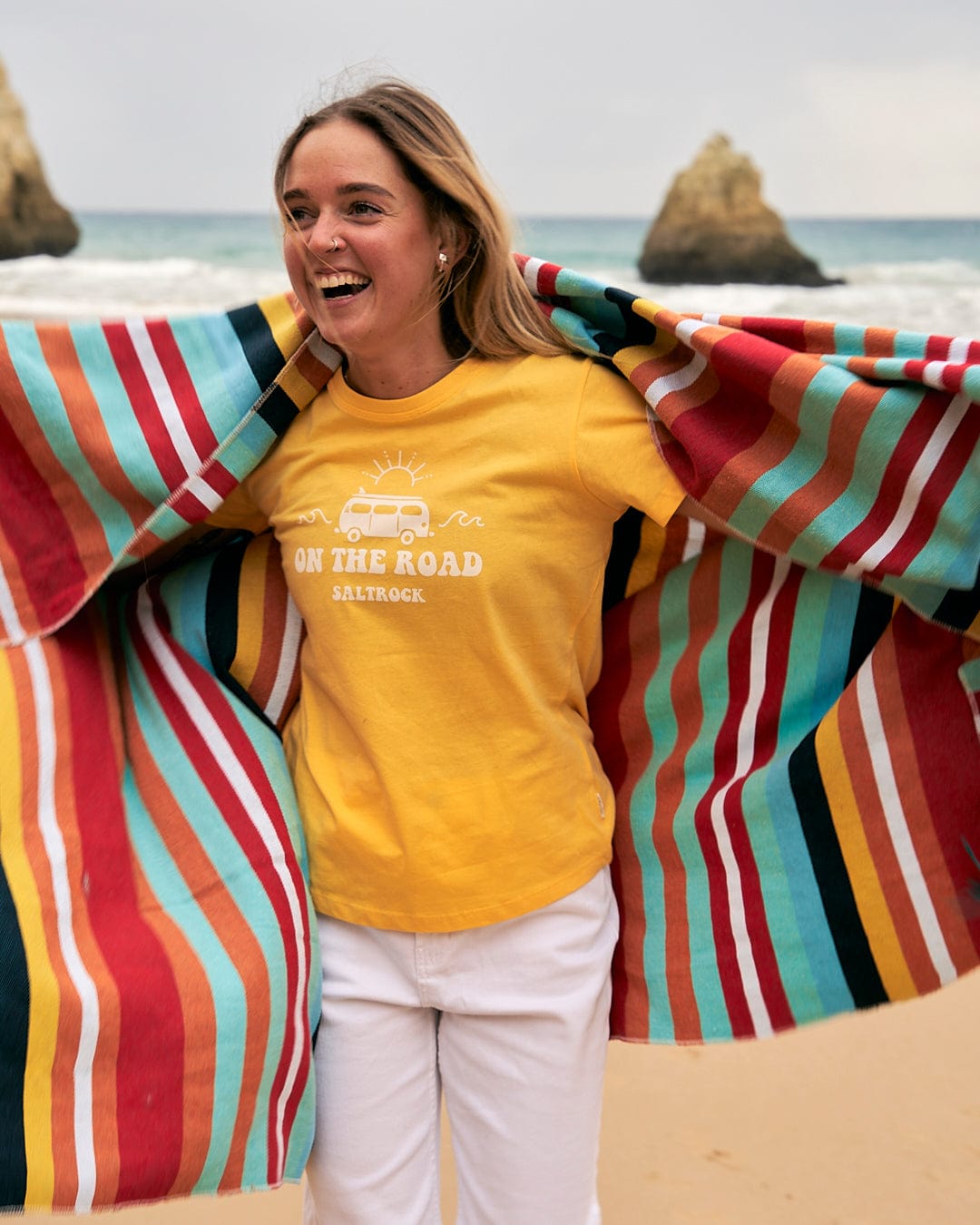 A woman wearing a yellow t-shirt holding a Saltrock Recycled Picnic Blanket - Multi on the beach.