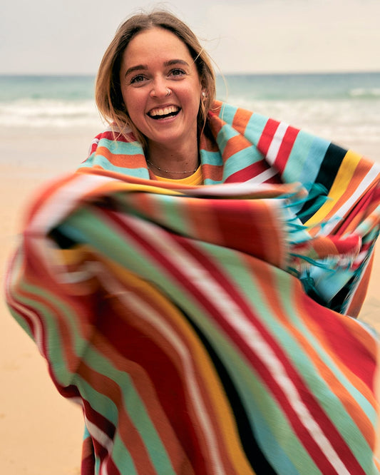 A woman is holding a Saltrock Recycled Picnic Blanket - Multi on the beach.