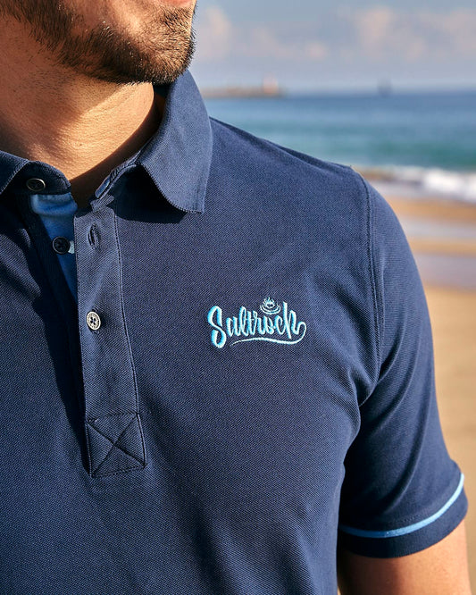 A man wearing a Roland - Mens Short Sleeve Polo Shirt - Blue by Saltrock on the beach.