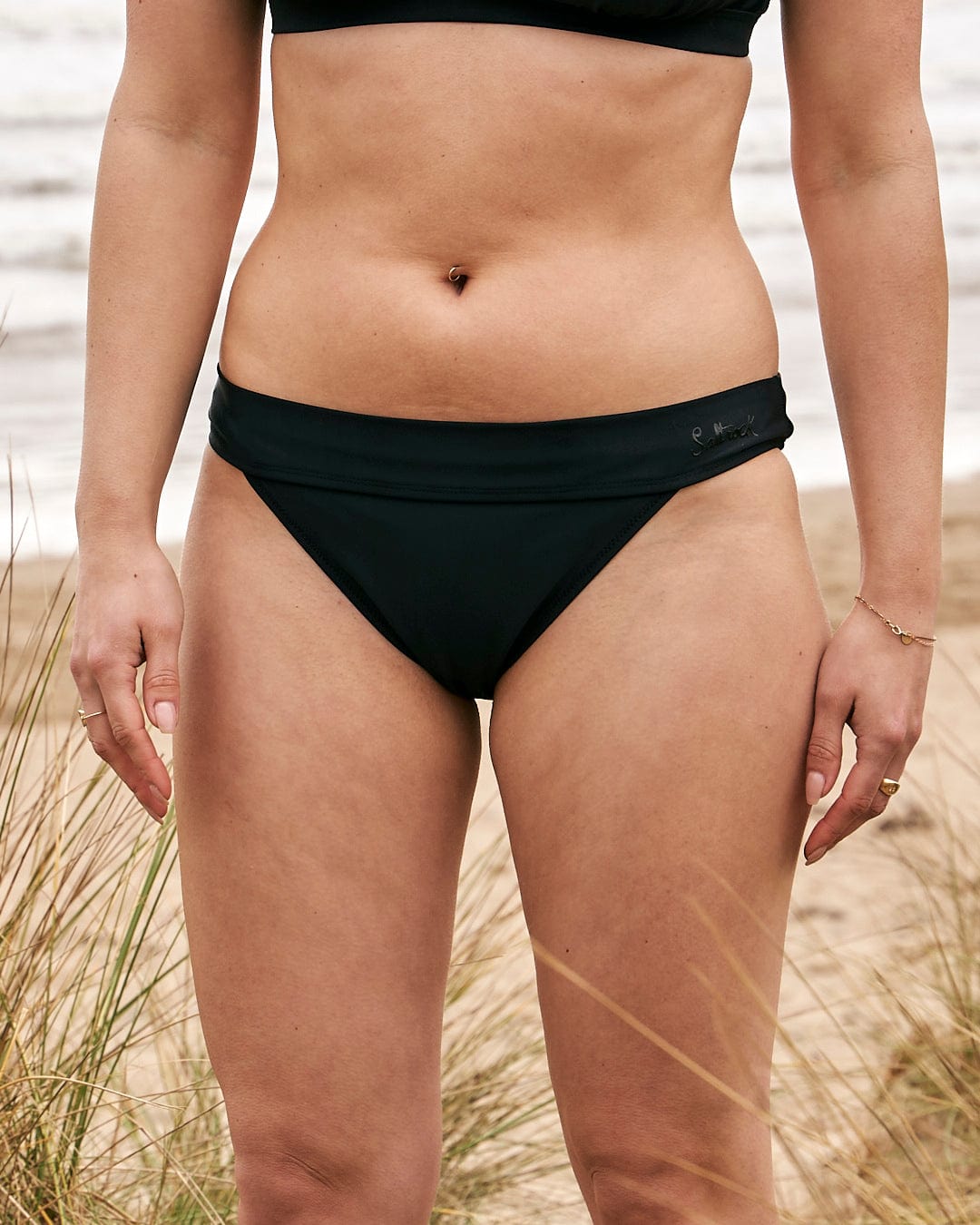 A woman in a Rosie - Womens Bikini Bottom - Black from Saltrock standing on the beach.
