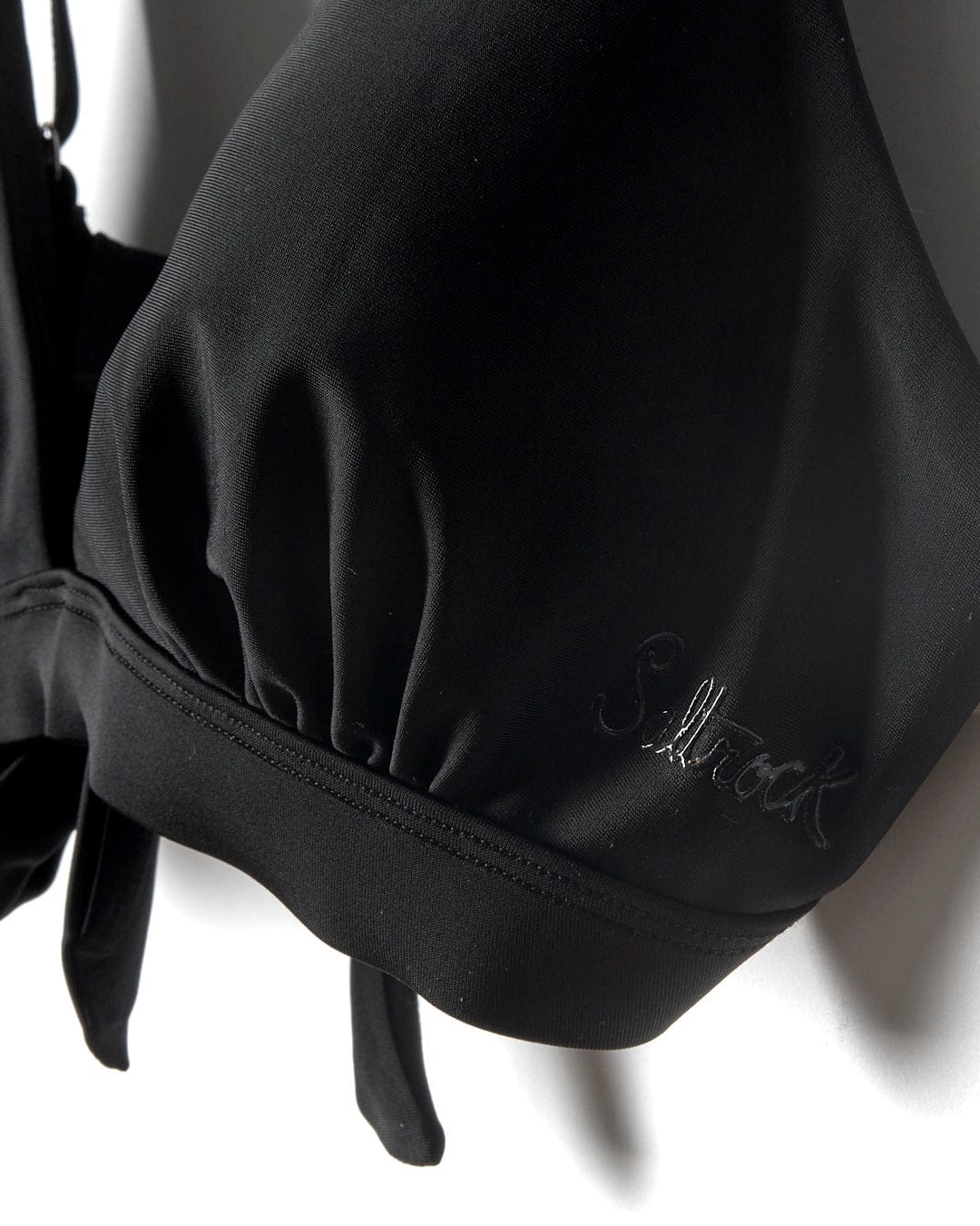 A durable Saltrock Rosie - Womens Bikini Top - Black with adjustable straps hanging on a white wall.