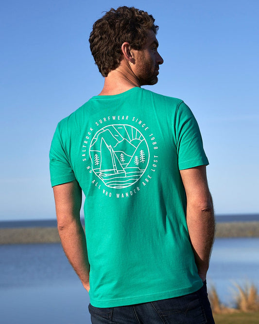 A man wearing a Saltrock Sailaway Outline - Mens Short Sleeve T-Shirt - Bright Green looking at the water.