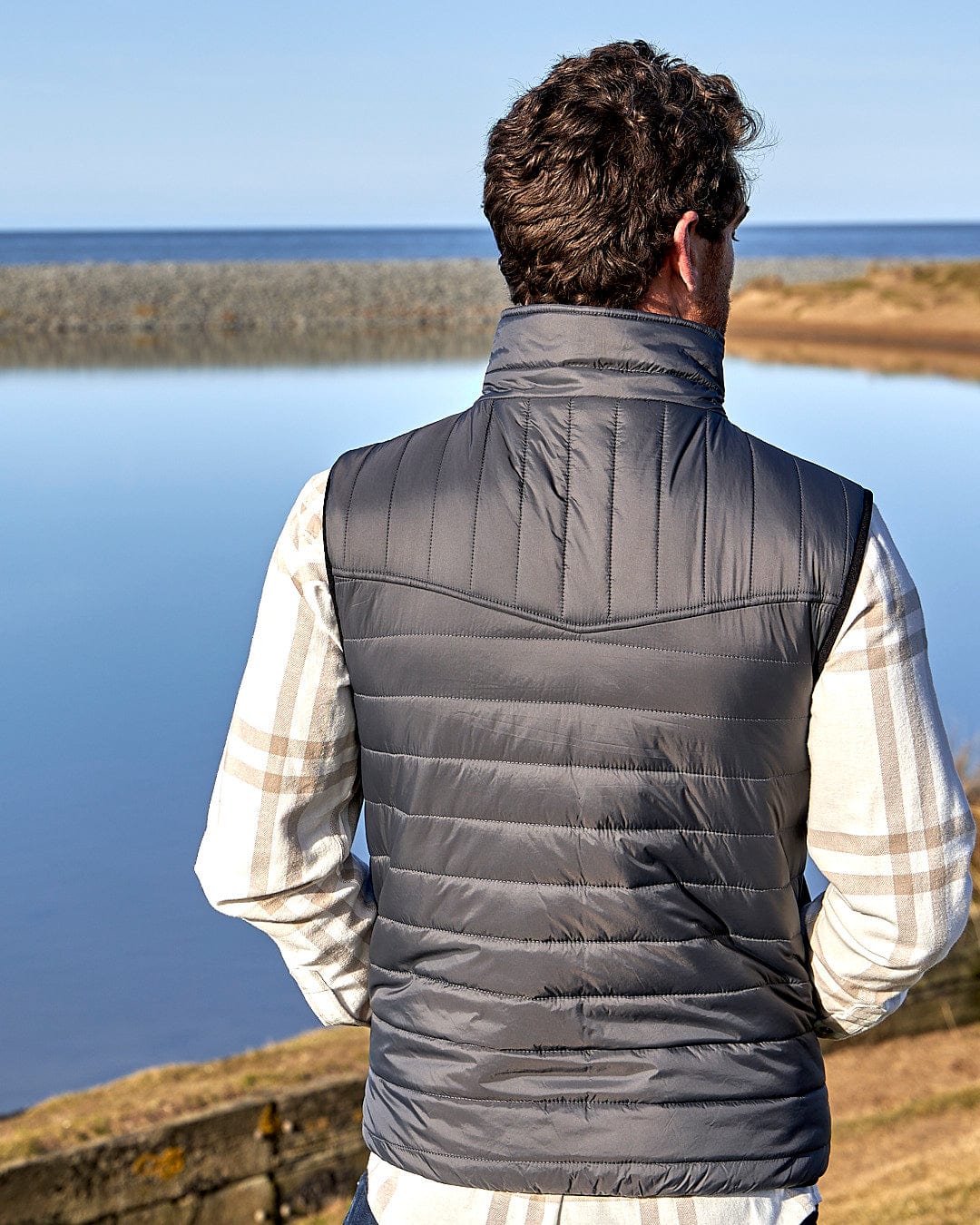 A man standing by a body of water wearing a Saltrock - Mens Reversible Gilet - Dark Green/Black vest.