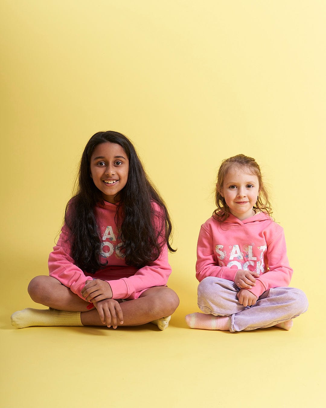 Two little girls sitting on the floor in Saltrock's Seabed - Kids Pop Hoodie - Pink sweatshirts.