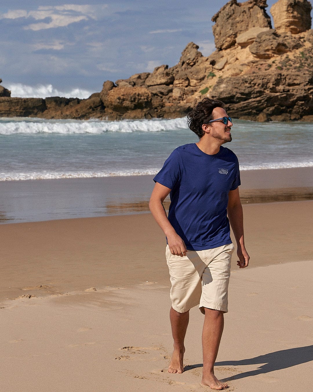 A man wearing a Saltrock Sennen - Mens Chino Short - Natural walking on a beach.
