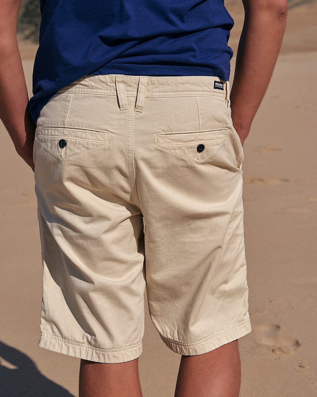 A man standing on a beach wearing Sennen - Mens Chino Shorts in Natural by Saltrock.