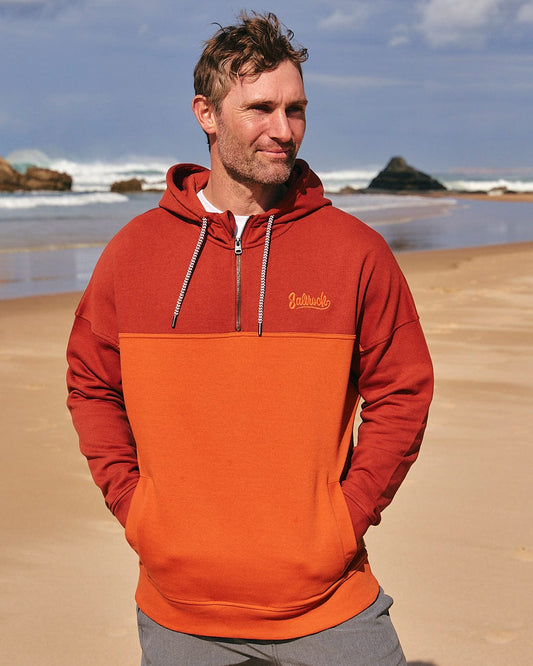 A man standing on a beach wearing a Saltrock Speed Embroidery - Mens 1/4 Neck Zip - Red hoodie.