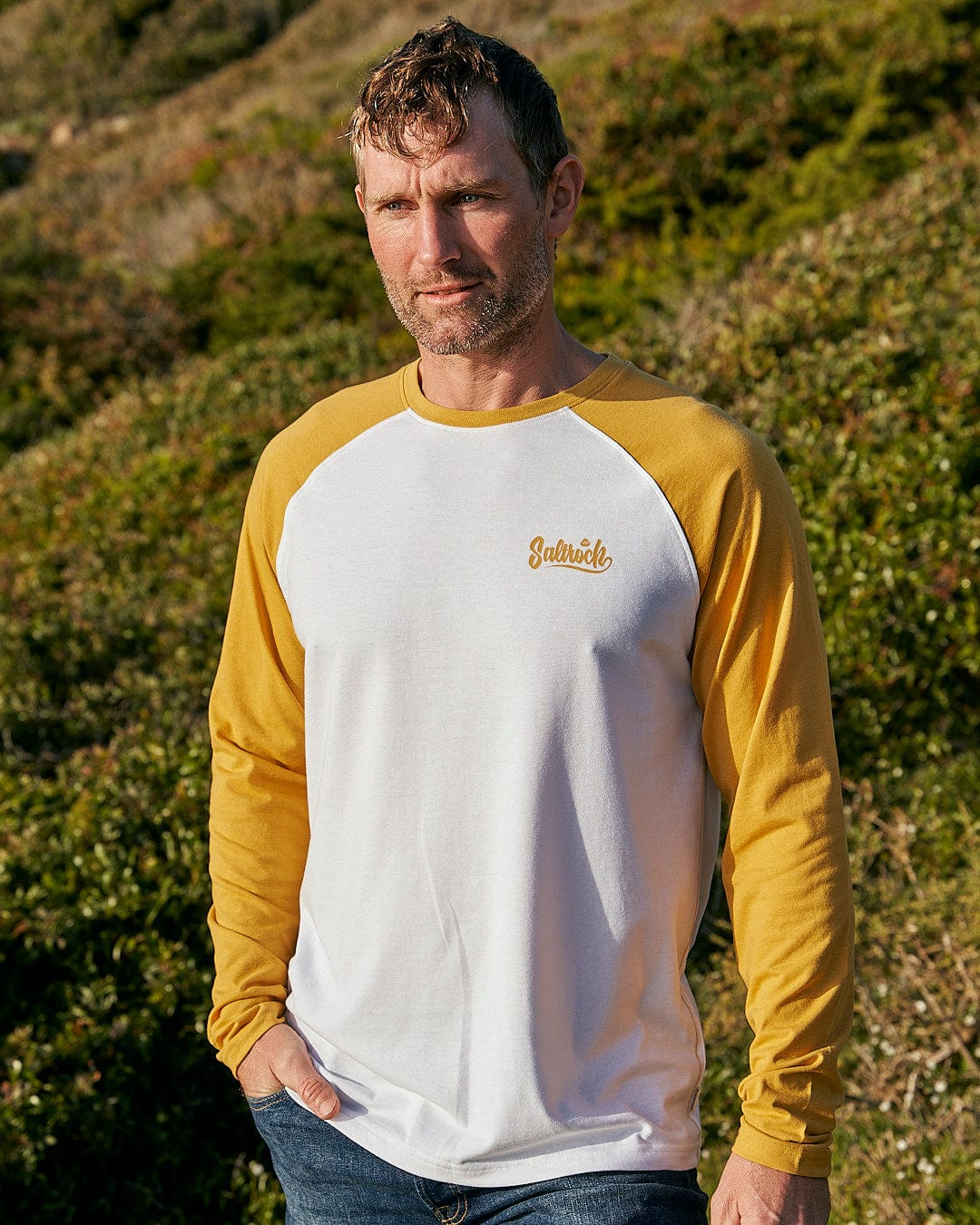 A man wearing a Saltrock Speed - Men's Long Sleeve Raglan T-Shirt in Ochre/White.