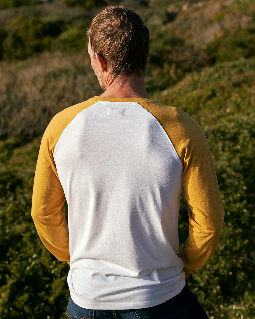 The back of a man wearing a Saltrock Speed - Mens Long Sleeve Raglan T-Shirt - Ochre/White.