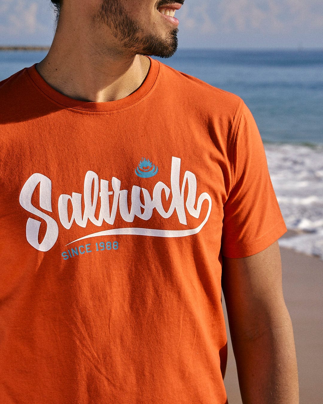 A man wearing a Saltrock Speed - Mens Short Sleeve T-Shirt - Red on the beach.