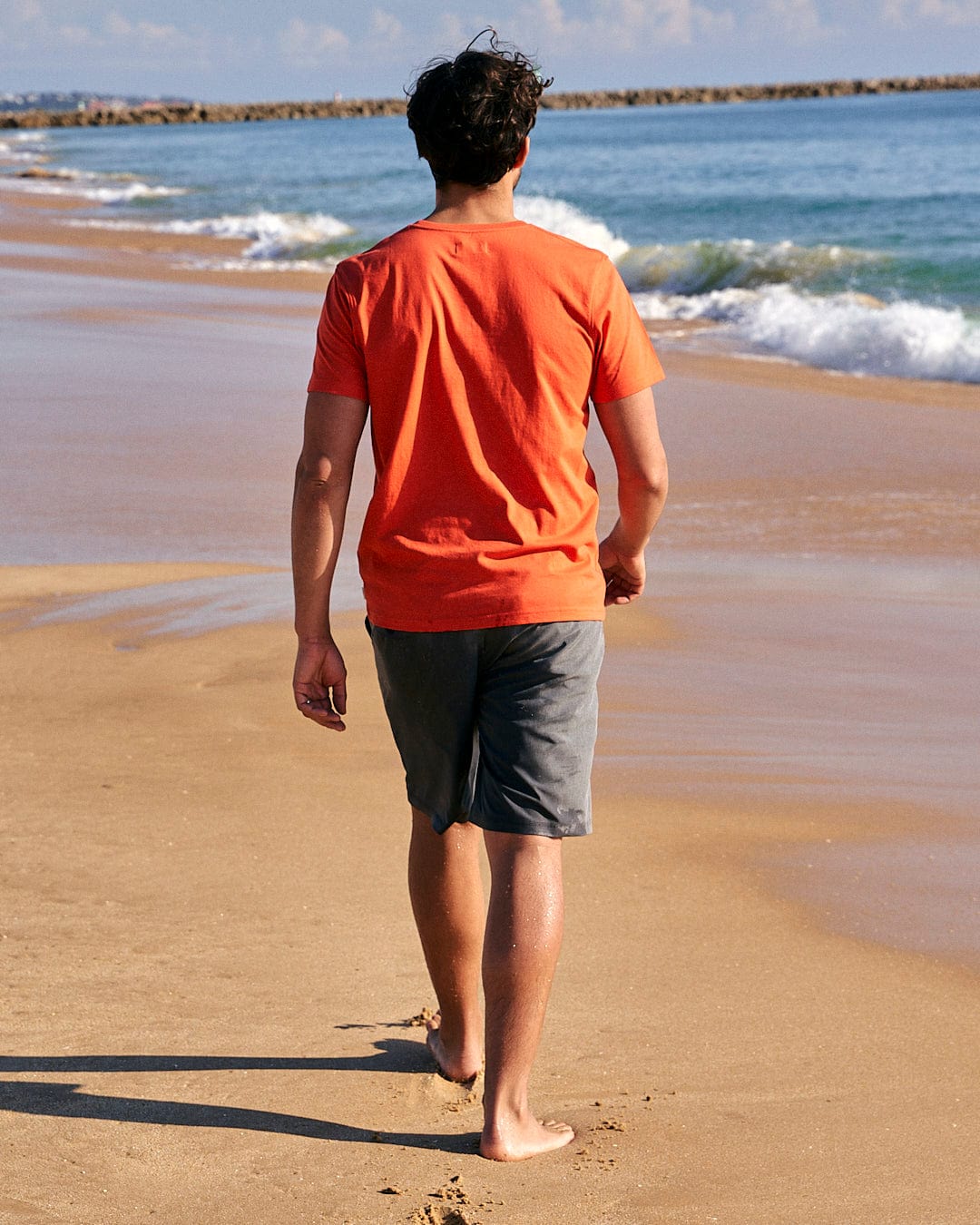 A man walking on a beach with a Saltrock Speed - Mens Short Sleeve T-Shirt in Red.
