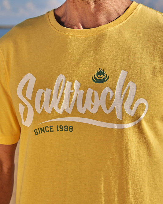 A man wearing a yellow Speed - Mens Short Sleeve T-Shirt with the word Saltrock on it.