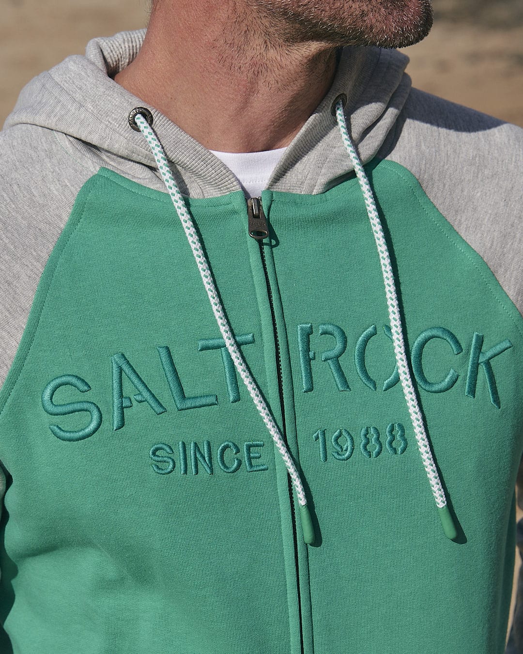 A man wearing a green and grey hoodie with the word Saltrock Stencil - Mens Zip Hoodie - Green on it.