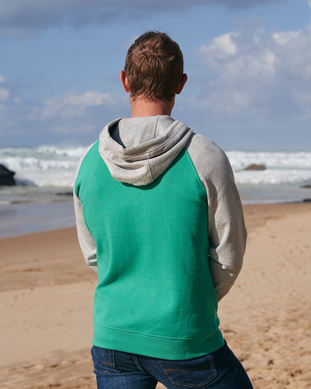 A man standing on a beach with his back to the ocean wearing a Saltrock Stencil - Mens Zip Hoodie - Green.