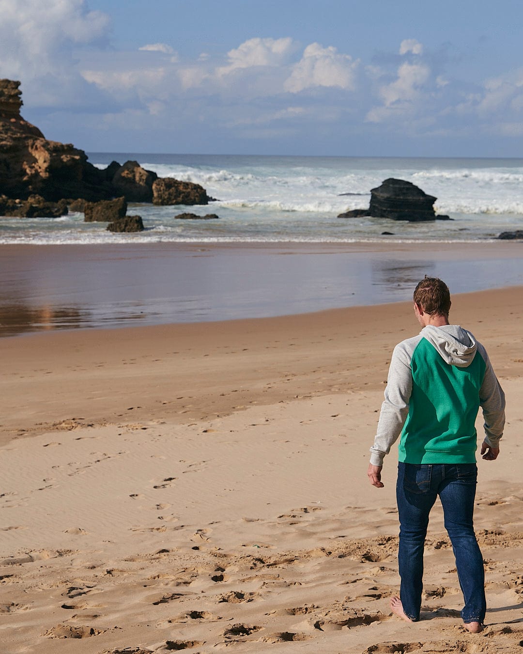 A man standing on a beach with a Saltrock - Stencil Mens Zip Hoodie - Green.