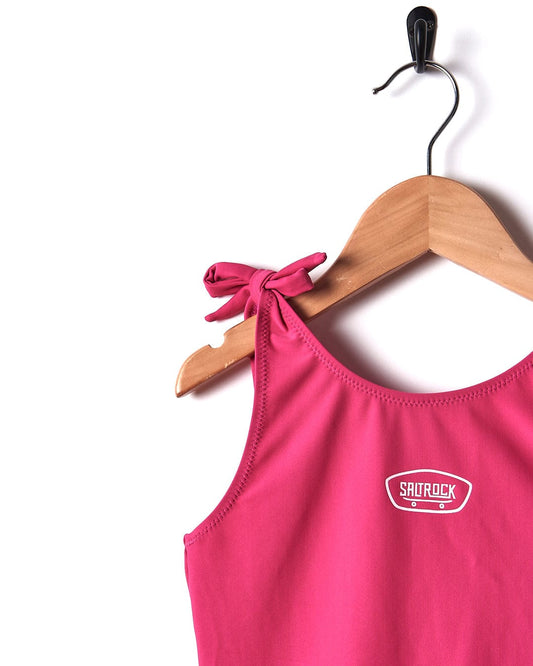 A Sunny - Kids Swimsuit - Pink hanging on a wooden hanger. (Brand: Saltrock)