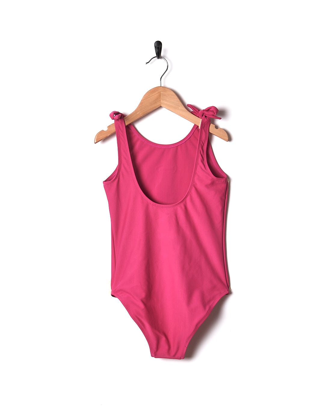 A Sunny Kids Swimsuit in Pink color hanging on a wooden hanger, by Saltrock.