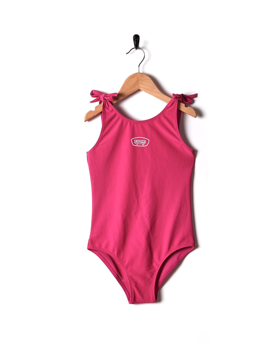 A Sunny - Kids Swimsuit - Pink from Saltrock hanging on a wooden hanger.