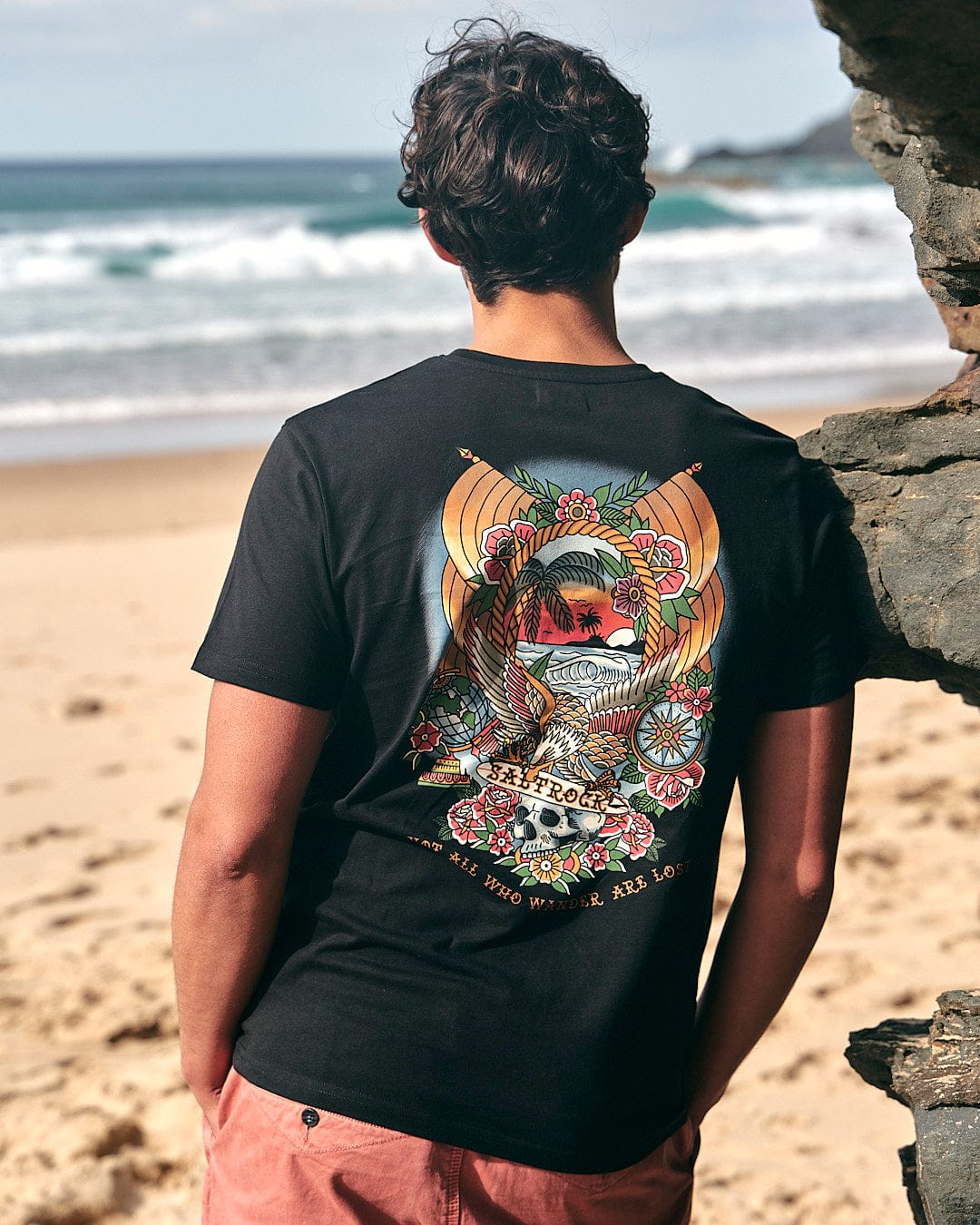 A man wearing a Saltrock - Tattoo Island Mens Short Sleeve T-Shirt in Black, looking at the ocean.