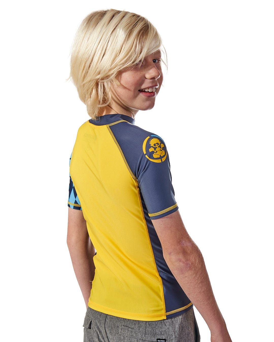 A young boy wearing a Saltrock Warp Kids Short Sleeve Rashvest - Yellow.