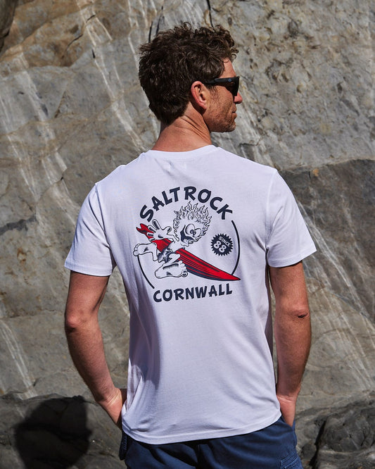 A man wearing a Saltrock Wave Rider Cornwall - Mens Short Sleeve - White t-shirt in front of a rock.