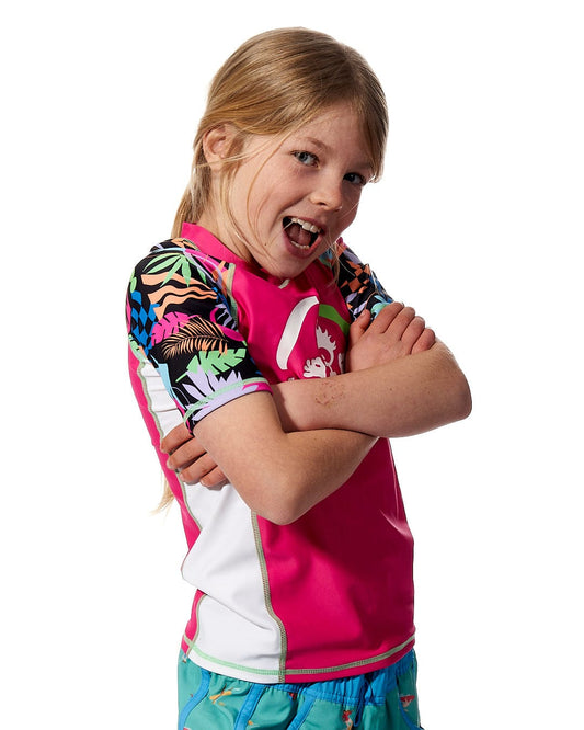 A young girl wearing a Saltrock Zephyr - Kids UPF 50+ Short Sleeve Rashvest in Pink, providing sun protection, posing for a photo.